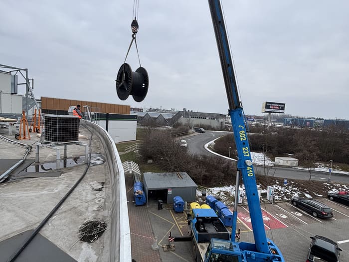 Autojeřáb zvedá kabelový buben na střechu objektu