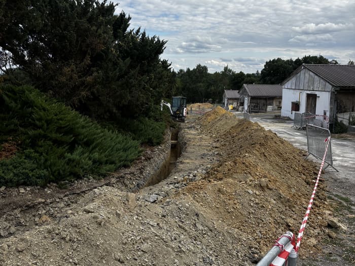 Výkop kabelové trasy vedoucí areálem farmy, v pozadí rýpadlo